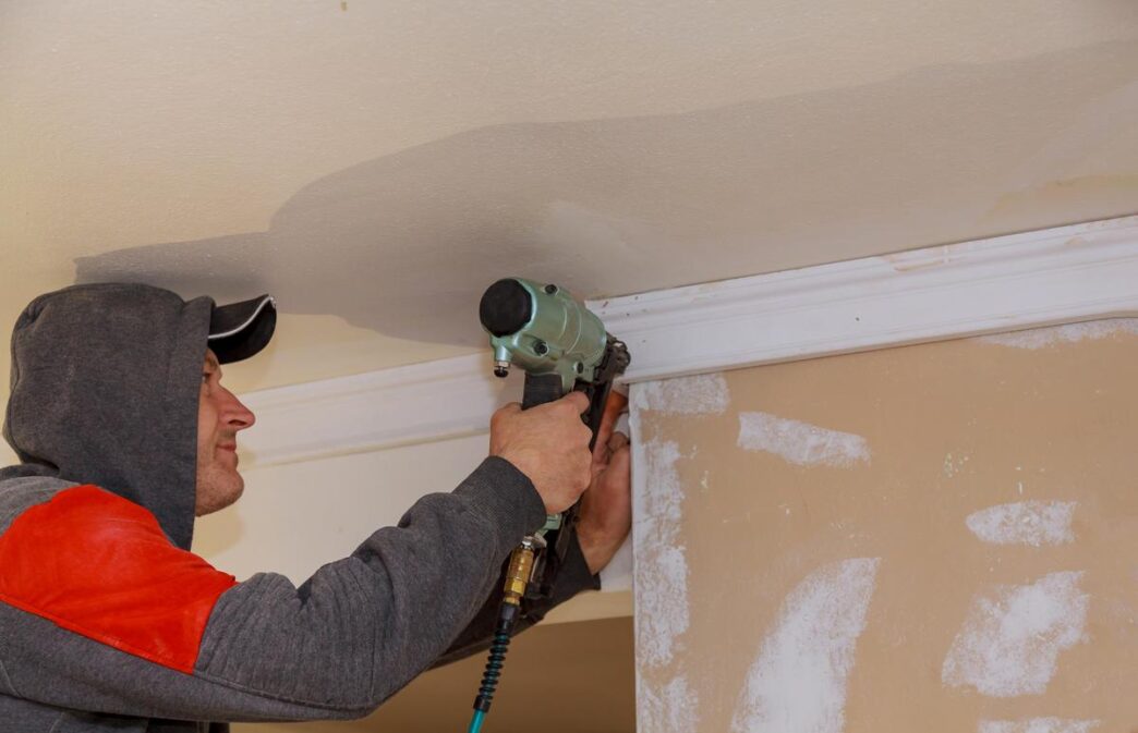 DIY enthusiast installing crown molding in a beautifully decorated living room, surrounded by tools.